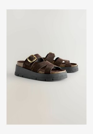 Braune Wildledersandalen mit breiten, überkreuzten Riemen und einem goldenen Schnallen-Detail. Korkeinlage auf einer dicken, schwarzen Gummiplattformsohle.