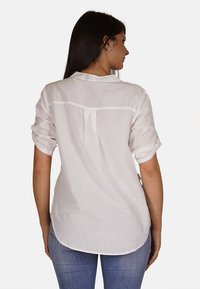 Camicia di lino bianca con maniche corte arrotolate, dettaglio del giogo posteriore e orlo curvo, abbinata a jeans in denim blu.