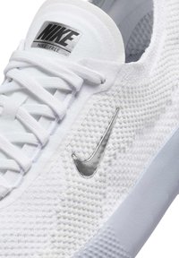 Sneakers Nike Free z białą, oddychającą siateczką, teksturowaną powierzchnią, płaskimi białymi sznurówkami oraz odblaskowym, srebrnym logo Swoosh.