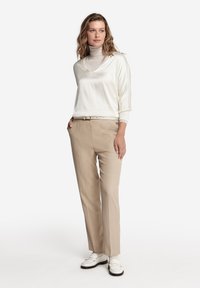 Top bianco a maniche lunghe con scollatura a V abbinato a pantaloni beige su misura e mocassini bianchi. Tessuto morbido e design slim fit.