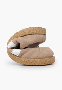 Pantofole beige in suede con forma curva, accenti bianchi e suola in gomma textured. Materiale morbido per comfort e flessibilità.