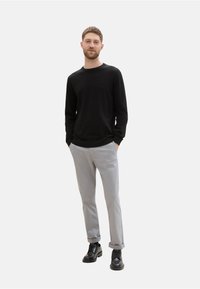 Schwarzer Langarmpullover mit gerippten Bündchen, kombiniert mit hellgrauen Hosen. Getragen mit schwarzen Schnürschuhen. Einfaches Design, neutrale Farben.