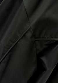 Svart tyg med en slät, matt textur, med kontrasterande sömmar och en närbild av sömnadsdetaljer.