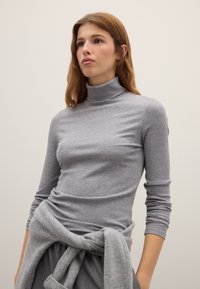 Graues, geripptes Rollkragenshirt mit langen Ärmeln. Glatte Textur. Hellgrauer Pullover um die Taille gebunden. Einfaches, figurbetontes Design.