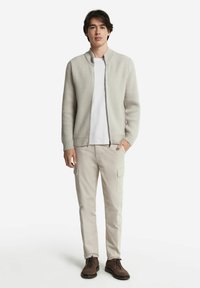 Ljusgrå ribbad cardigan med dragkedja fram, i kombination med beige cargobyxor och mörkbruna snörskor. Enkel design, texturerad stickning.