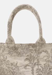 Beige textured tote bag met een geweven stof met een door de natuur geïnspireerd patroon. Twee stevige, ronde handvatten zijn aan de bovenkant bevestigd.