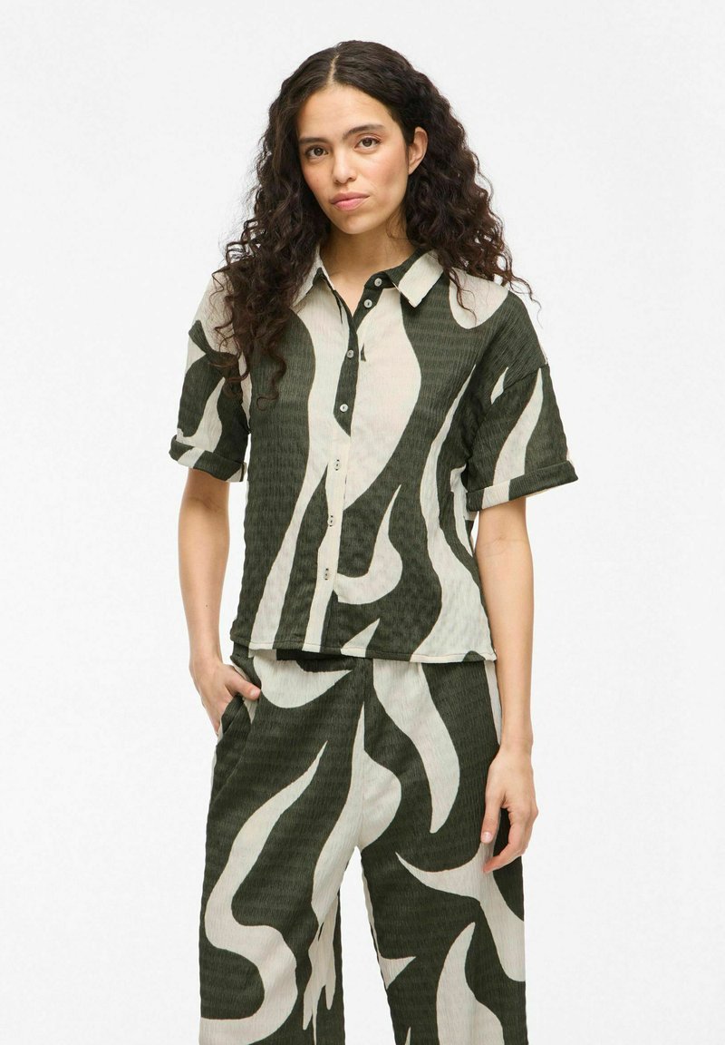Button-up shirt and matching pants featuring a green and beige abstract pattern. Textured fabric with rolled sleeves and loose fit.