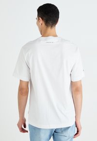 Camiseta de algodón blanca con mangas cortas, cuello redondo y un detalle impreso "LONDON W11" en la parte superior de la espalda. Combinada con jeans azul claro.