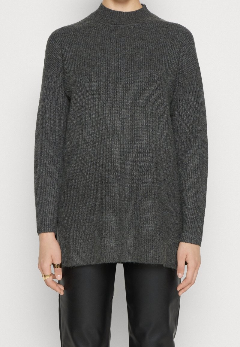 Dunkelgrauer gestrickter Pullover mit hohem Kragen, gerippter Textur, langen Ärmeln und lockerer Passform, kombiniert mit schwarzen Lederhosen.