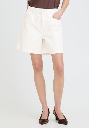 Frau trägt weiße Shorts mit hoher Taille und Taschen, kombiniert mit braunen Slingback-Pumps mit Leopardenmuster.