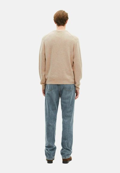 Sudadera beige con cuello redondo y puños acanalados, combinada con vaqueros de pierna recta azul claros y calzado oscuro. Textura sutil visible.