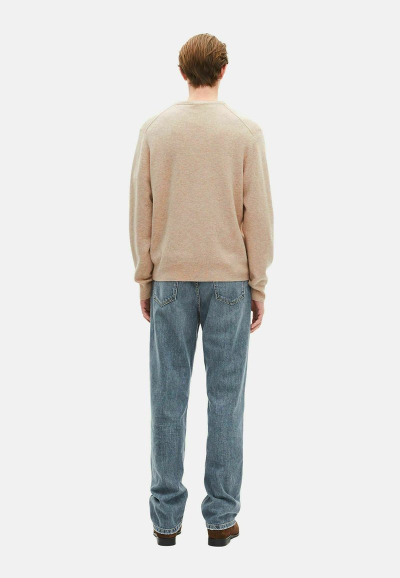 Beige Sweatshirt mit Rundhalsausschnitt und gerippten Bündchen, kombiniert mit hellblauen geraden Jeans und dunklem Schuhwerk. Subtile Textur sichtbar.