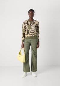 Pull en maille avec des motifs géométriques dans des tons terreux ; pantalon vert olive ; sac à main jaune vif ; baskets blanches.