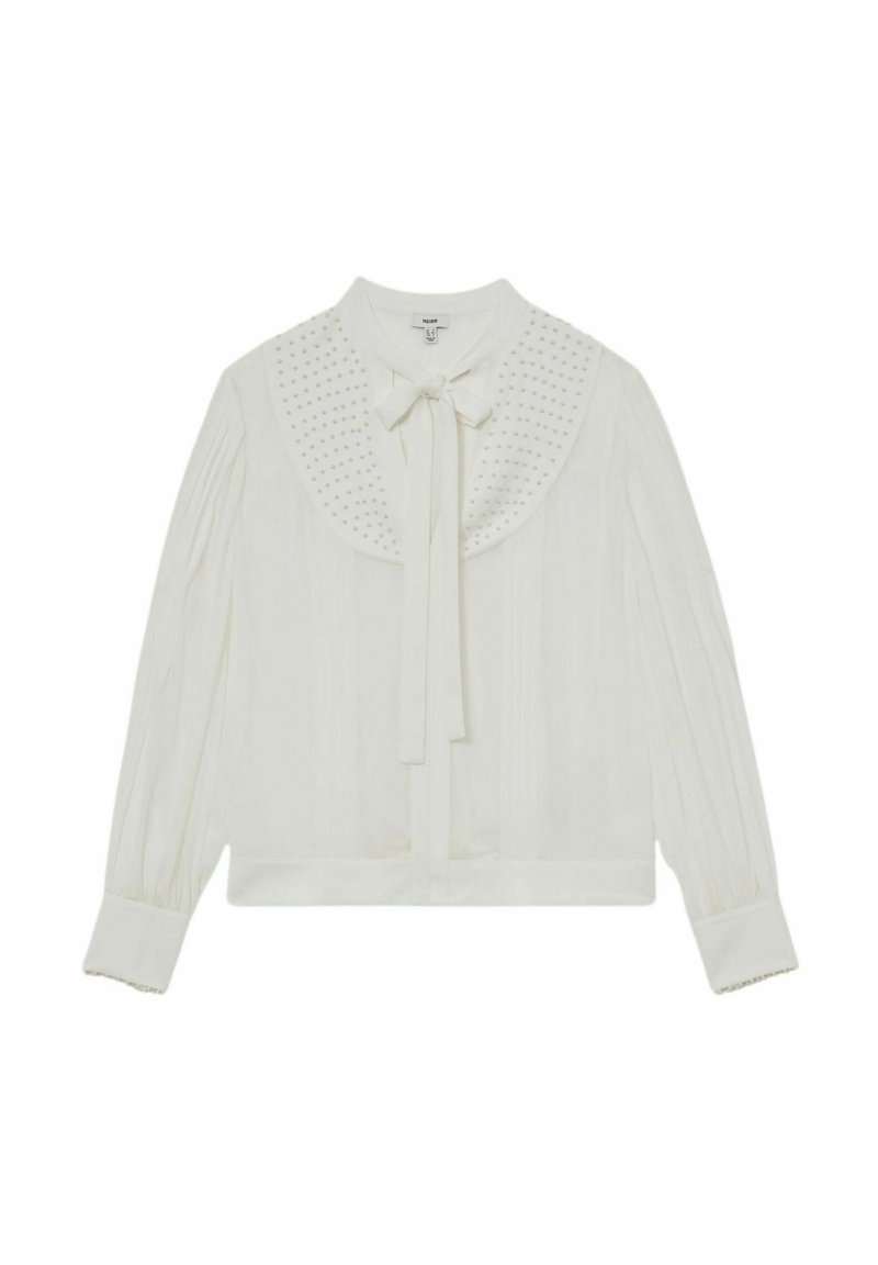 Hvid bluse med lange ærmer med plisserede ærmer, bred krave pyntet med små nitter og en sløjfe ved halsudskæringen.