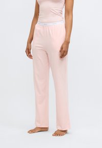 Világos rózsaszín pizsamanadrág, laza szabással, puha anyagból készült, rugalmas derékrésszel, fehér márkajellel. Zsebek nem láthatók.