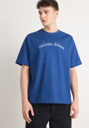 Blue cotton t-shirt with short sleeves and a loose fit, featuring white embroidered "calvin klein" text across the chest.