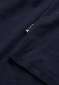 Laivastonsininen puuvillapaita, jossa on näkyvä logotägi sauman kohdalla, sileä pinta ja yksinkertainen muotoilu, jossa on taitettu hihansuu.