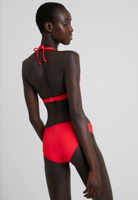 Roter Bikini-Set mit Halterneck und verstellbarem Bindeband, nahtlosem Bund und tief sitzenden Unterteilen, aus glattem, dehnbarem Material gefertigt.