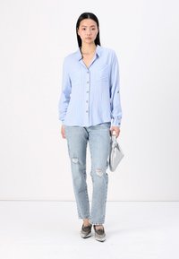Light blue, striped button-up shirt with two chest pockets and cuffed sleeves, paired with distressed light jeans and silver handbag.