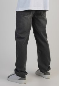 Jeans din denim negru cu o croială relaxată, având cinci buzunare și o ușoară decolorare. Asortați cu adidași albi cu accente gri.