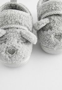Chaussons en peluche gris avec un extérieur texturé et duveteux, ornés d'oreilles de lapin et de détails en cœur brodés à l'avant, ainsi qu'une doublure à motifs à carreaux.