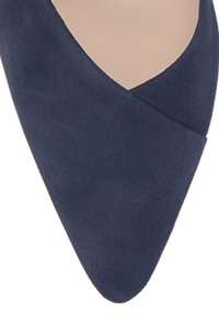 Marinblå mockaskor med hög klack, spetsig tå och en asymmetrisk skärning över ovandelen, som visar en slät textur.