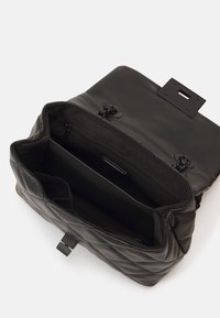 Černý prošívaný kožený batoh s horním víkem. Vnitřek obsahuje dvě přihrádky, jednu na zip. Součástí jsou kovové doplňky.