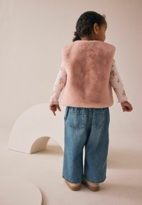 Faux-Fur-Weste in sanftem Rosa, kombiniert mit lockeren, hellblauen Denim-Jeans mit Gesäßtaschen, getragen mit beigen Schuhen. Einfaches Design.