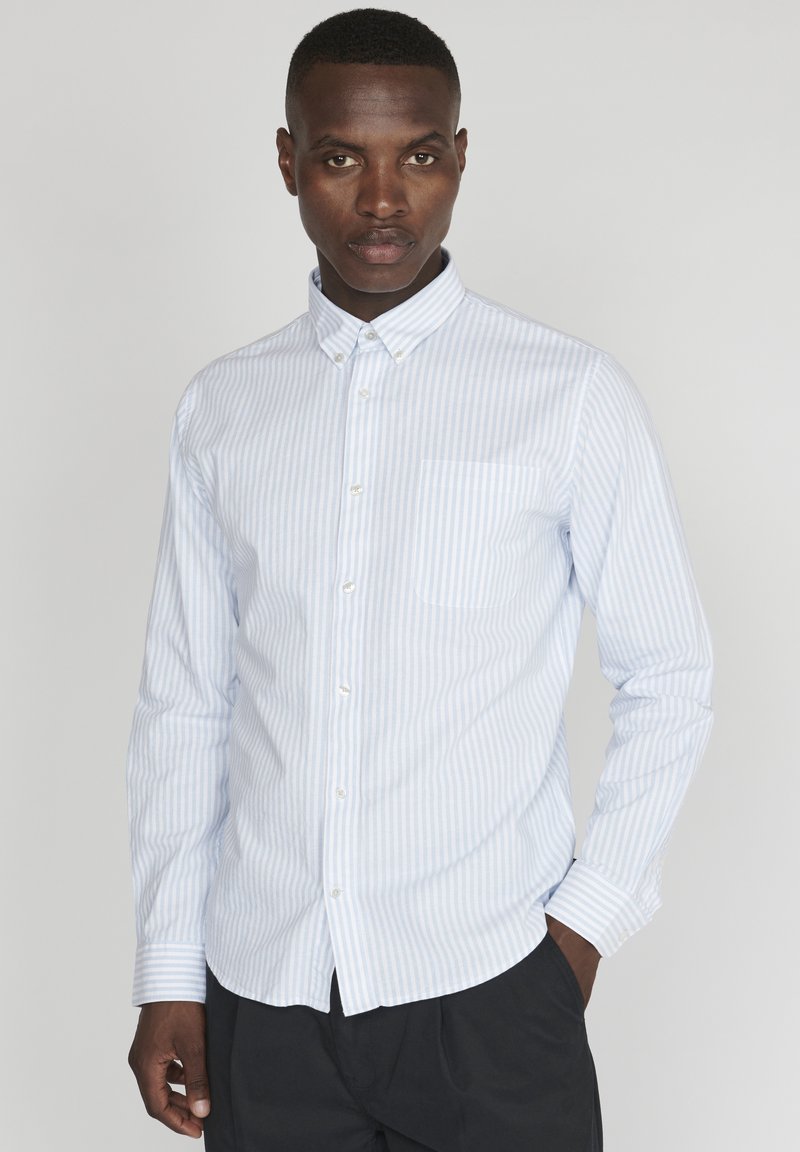 Camisa de botones a rayas azul claro y blanca con cuello y un bolsillo en el pecho. Tiene mangas largas y un corte ajustado.