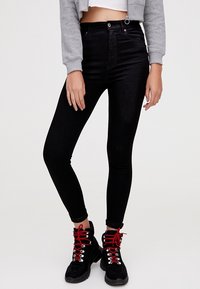 Jean noir taille haute en denim, avec une coupe ajustée. Associé à des bottes noires à lacets rouges et un sweat-shirt court gris.