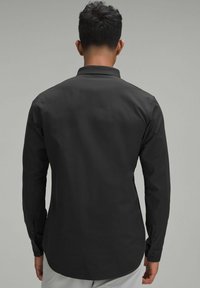 Maglietta nera a maniche lunghe realizzata in tessuto liscio; presenta un colletto classico e polsini con bottoni, con una cintura dritta e un design minimal.
