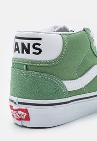 Baskets montantes Vans vertes et blanches montrant l’arrière avec le logo Vans noir sur la tige blanche et l’étiquette rouge Vans Off The Wall sur la semelle blanche.