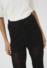Zwarte meshbroek met een geometrisch patroon, elastische tailleband met trekkoord en een getextureerde stof die ademend is.