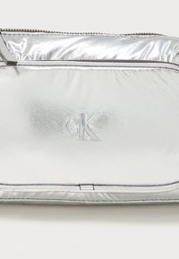 Silver pouch bag featuring a smooth, reflective finish, a zip closure, and embossed "cK" logo on the front. Slim, sleek design.