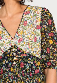 Blumenmuster-Kleid mit V-Ausschnitt, Puffärmeln und kontrastierenden Farbabchnitten in Weiß, Schwarz und lebhaften Farben. Mit Perlenakzenten.