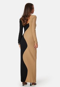 Abito lungo aderente con un motivo testurizzato. Presenta un lato nero e un lato beige con un design a blocchi di colore ondulato. Maniche lunghe e schiena a V.