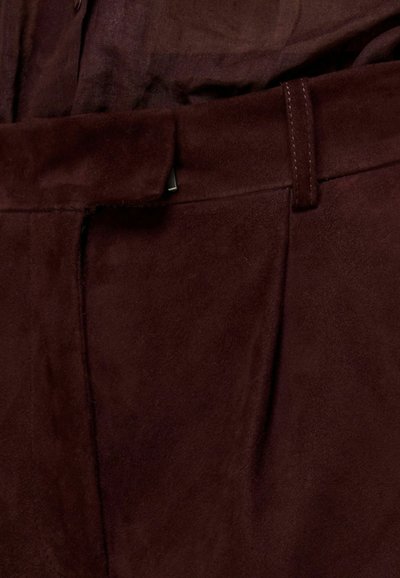 Pantaloni in suede borgogna con texture liscia, dotati di tasche laterali e passanti per cintura. Linee pulite e dettagli di cucitura tono su tono.