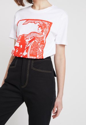 Biała koszulka z krótkim rękawem z czerwonym motywem kobiety w tradycyjnym stroju, zestawiona z czarnymi spodniami z wysokim stanem i kontrastowym przeszyciem.