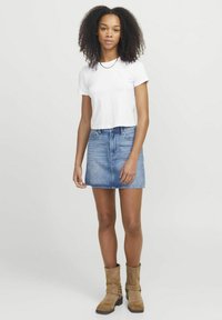 Hvit kort t-skjorte, blå denim mini skjørt, brune semsket ankelstøvler med spenne detaljer. Håret er krøllete og faller forbi skuldrene.