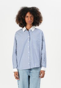 Camicia con bottoni, a righe verticali blu e bianche, colletto bianco a contrasto, maniche lunghe e taschino a sinistra sul petto. Design a taglio casual.