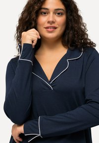 Maglietta a maniche lunghe blu navy con scollo a V e bordino bianco lungo il colletto e i polsini; realizzata in tessuto morbido e elasticizzato.