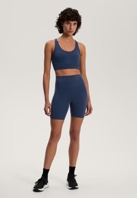 Sötétkék sportmelltartó és magas derekú, sima, rugalmas anyagból készült rövidnadrág, illeszkedő fazonnal és varrat nélküli kialakítással.