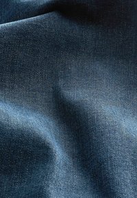 Dark blue denim fabric with a smooth texture and subtle sheen, displaying slight folds and creases, emphasizing its weave and durability.