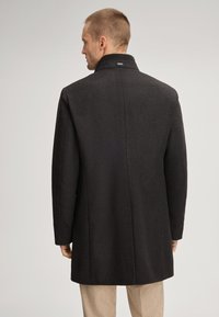 Dunkler Wollmantel mit hohem Kragen, der eine glatte Textur und einen geraden Schnitt aufweist. Die Rückansicht zeigt minimale Nähte und ein dezentes Markenetikett.