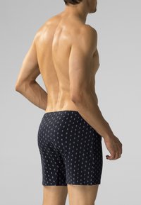 Granatowe kąpielówki wykonane z lekkiego materiału, z powtarzającym się geometrycznym wzorem. Mają dopasowany krój i elastyczny pas.