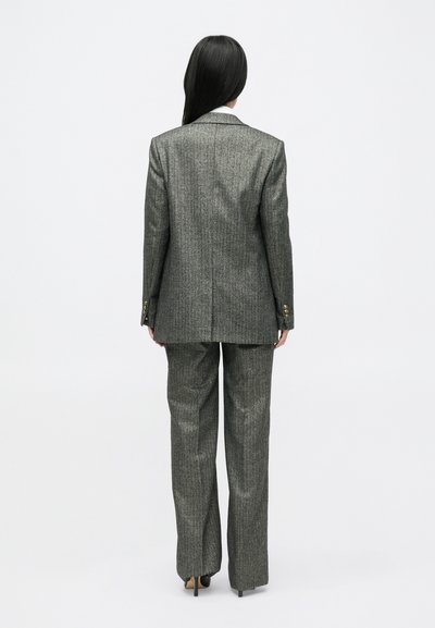 Pilkas smėlinis kostiumas su pritaikytu švarku ir plačiomis kelnėmis, su tekstūruotu audiniu ir auksinėmis mygtukų detalėmis.