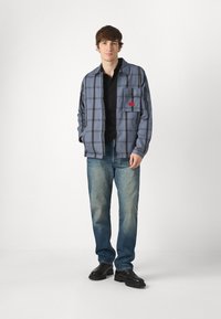 Rutete skjorte i grå og blå, med brystlomme; kombinert med falmede blå jeans og svarte støvler. Glatt tekstur, avslappet passform.