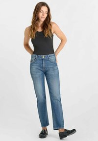 Blauwe spijkerbroek met een rechte pasvorm, voorzien van een middelhoge taille, een metalen knoopsluiting en een vijf-pocket ontwerp. Gecombineerd met een zwarte tanktop.