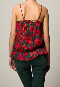 Röd blommig linne med tunna axelband, med en rynkad rygg och peplum-kant. Matchad med mörkgröna figurnära byxor.