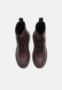 Botas de tornozelo em couro burgundy com biqueiras redondas, atacadores pretos e linguetas; apresentam uma sola texturizada e um detalhe de costura contrastante.